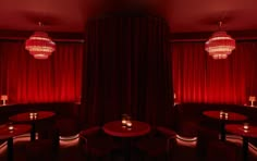 a dimly lit room with red curtains and round tables