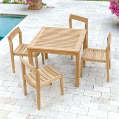 a wooden table and chairs next to a swimming pool with pink flowers in the background