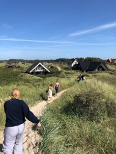 several people walking down a path in the sand dunes near some houses and grass on a sunny day