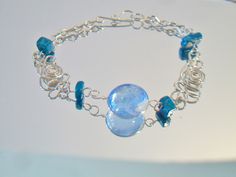 Blue beaded wire bracelet. It measures approx. 7 inches long and has a hook closure. Made with a round cornflower blue glass cabochon in the center, 4 deep turquoise blue glass square beads and swirling Peruvian Alpaca Silver wire chain. Handmade, delicate and light weight. Add it to your jewelry wardrobe. All sales are final and as is. Thank you for looking. You may also love this: https://www.etsy.com/listing/236165636/red-murano-glass-tear-drop-earrings-hoop?ga_search_query=murano&ref=sho Modern Turquoise Glass Jewelry, Blue Wire Wrapped Bracelets With Round Beads, Blue Wire Wrapped Bracelet With Round Beads, Blue Glass Bracelet Jewelry, Blue Wire Wrapped Bracelets, Wire Wrapped Round Glass Beads Jewelry, Wire Wrapped Glass Round Beads Jewelry, Unique Blue Wire-wrapped Bracelets, Turquoise Glass Round Jewelry