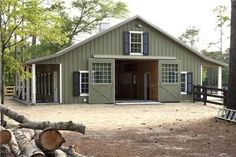 there is a barn with lots of logs in front of it and trees around the yard