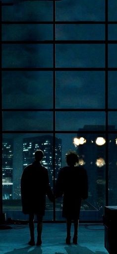 two people standing in front of a window at night with the city lights lit up