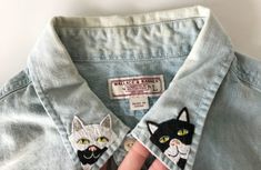 a person wearing a cat patch on their left chest and right hand in the pocket of a light blue jean shirt