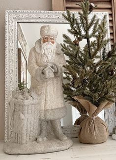 a statue of santa holding a sack next to a christmas tree in front of a mirror