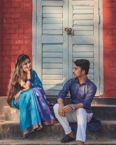 a man and woman sitting on steps in front of a red brick building with shutters