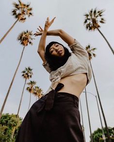 a woman standing in front of palm trees reaching up to catch a frisbee