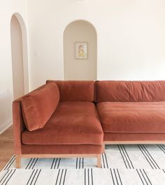 an orange couch sitting on top of a wooden floor next to a white and black striped rug