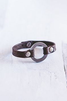 a close up of a leather bracelet on a white surface with a metal ring in the middle