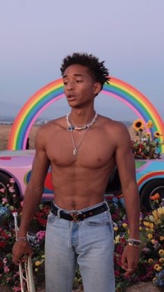 a shirtless man standing in front of a car with a rainbow painted on it