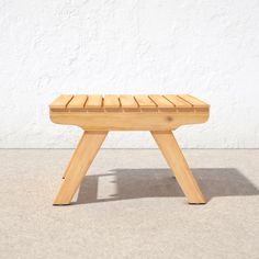 a wooden bench sitting on top of a cement floor next to a white wall,