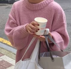 a woman in pink sweater holding coffee cup and shopping bag