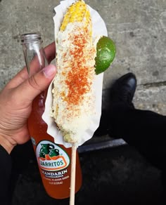 a person holding a hot dog on a stick with ketchup and sour cream