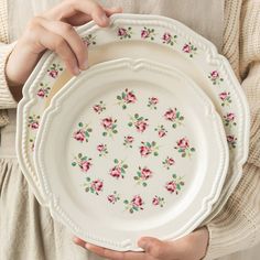 a woman holding two plates with pink flowers on them, one is white and the other is green