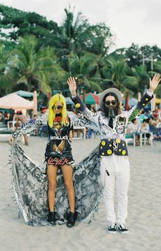 two people standing on the beach with their arms in the air and one person wearing a costume