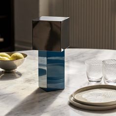 a table with plates and glasses on it, next to a silver cube shaped object