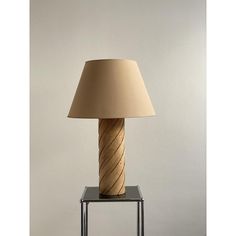 a lamp that is sitting on top of a glass stand with a beige shade over it