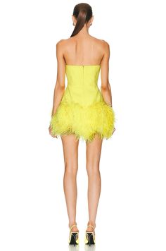 a woman wearing a yellow dress with ostrich feathers on the skirt and heels