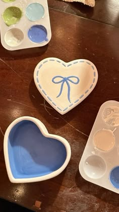 two heart shaped dishes and one with a blue bow on it sitting on a table