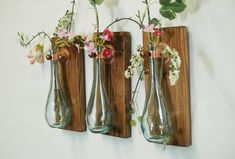 three vases with flowers in them are hanging on a wooden board and one is empty