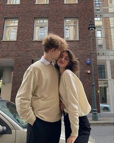 a man and woman standing next to each other in front of a tall brick building