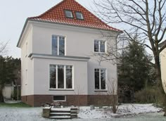 a white house with red tiled roof and windows in the front yard covered in snow