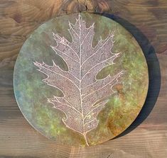 a metal plate with a leaf etched on the front and side, sitting on a wooden surface