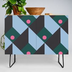 a plant is sitting on top of a cabinet with geometric designs and pink polka dots