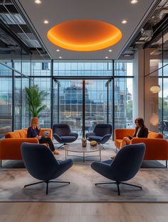 two women are sitting in an office lobby with orange and blue chairs, while one woman is on her cell phone