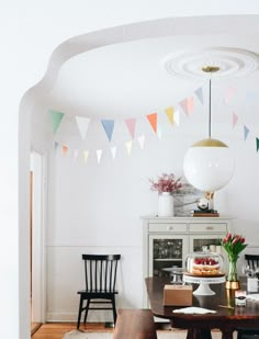 a dining room table with cake on it and bunting flags hanging from the ceiling