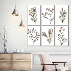 four floral paintings hanging on the wall above a chair in a white room with a wooden dresser