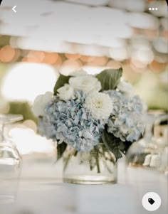 a glass vase filled with blue and white flowers on top of a table next to glasses