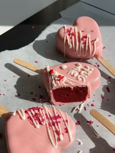 pink cake pops with white icing and sprinkles on them, one half eaten