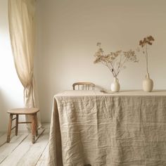 two vases with flowers sit on a table in front of a curtained window