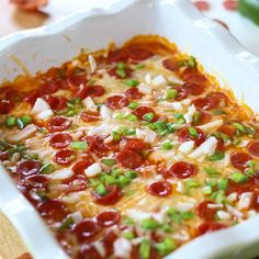 a square casserole dish with pepperoni and green onions on the top, topped with cheese