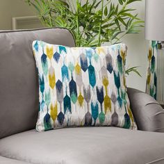 a gray couch with a blue and yellow pillow on it next to a potted plant