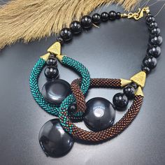 two necklaces with black beads and tassels on top of a gray surface