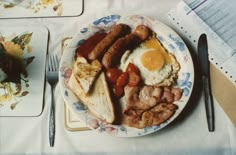 a plate with eggs, sausages and other food on it next to silverware