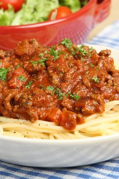 pasta with meat and tomato sauce on a plate next to a bowl of lettuce