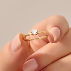 a woman's hand holding a gold ring with a white diamond on the middle