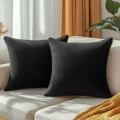 two black pillows sitting on top of a white couch next to a potted plant