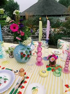 the table is set with plates, candles and flowers in vases on striped cloth