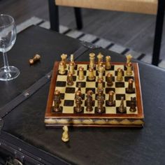 a chess board and some wine glasses on a table with a chair in the background