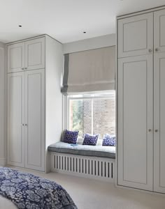 a bedroom with white cupboards and a window seat in the corner next to it