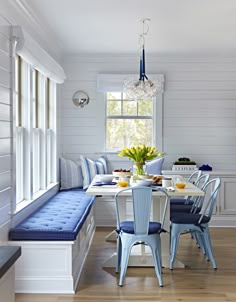 the dining room table has blue chairs and is next to a breakfast nook with built - in benches