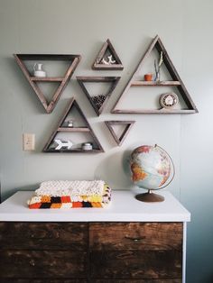 three triangular shelves on the wall above a dresser with a small globe and other items