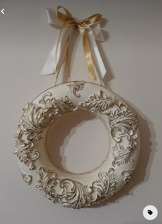 a white wreath hanging on the wall with a ribbon around it and a bow attached to it