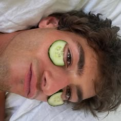 a man laying in bed with cucumber slices on his face and eyes,