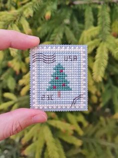 someone is holding up a small cross stitch christmas tree ornament in their hand