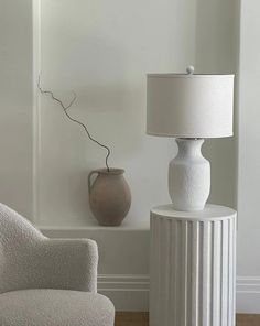 a white table lamp sitting next to a chair