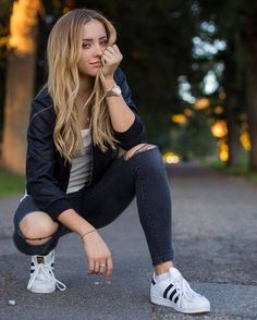 a young woman sitting on the ground with her hand under her chin and looking at the camera